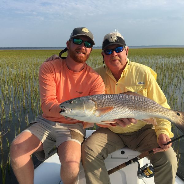 Two anglers holding a redfish in the marsh